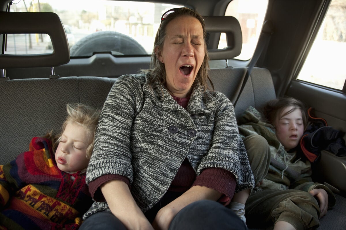 Exhausted mother yawns while her daughters sleep.