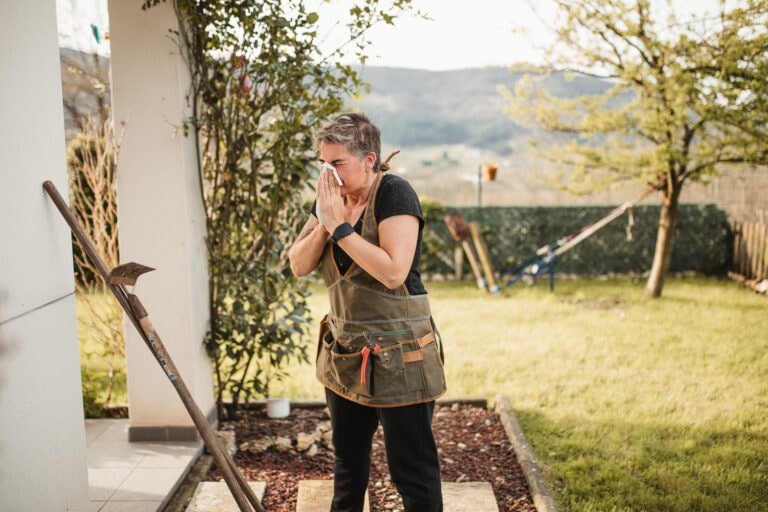 adult woman suffering from spring allergy and blowing a runny nose with a tissue while working in the garden