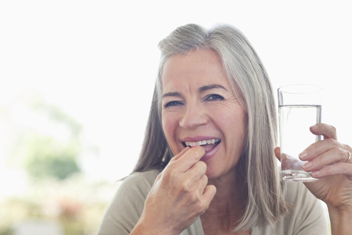 Woman holding glass of water taking pill