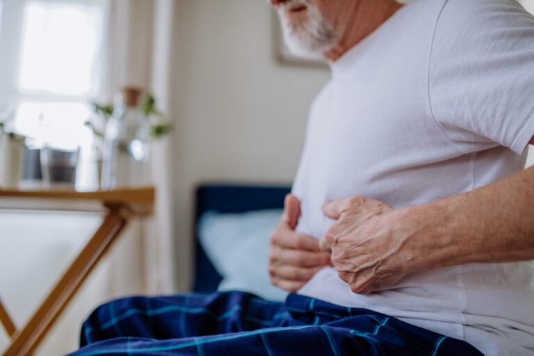 Senior man with stomach pain sitting in bed.