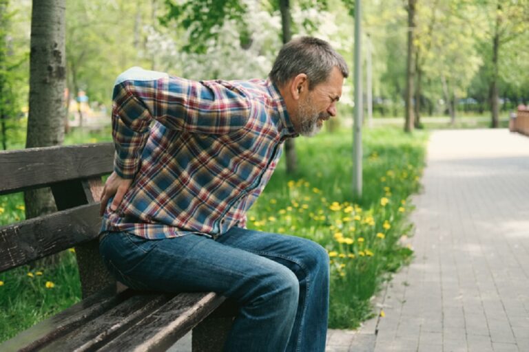 Suffering man holding his back in spring park.