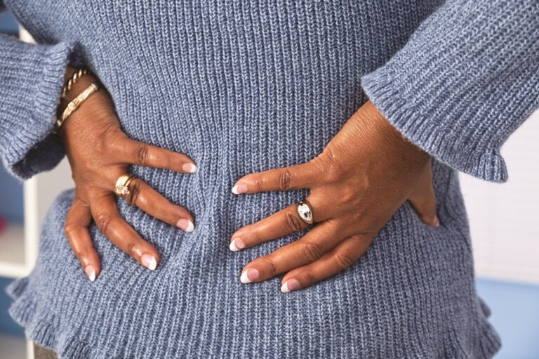 Senior African descent woman grabs lower back in pain