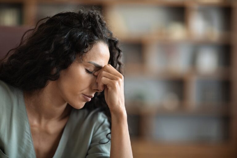 Upset brunette curly woman suffering from headache while working