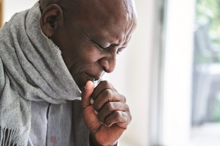 Senior African-American man wearing a scarf and coughing in his hand