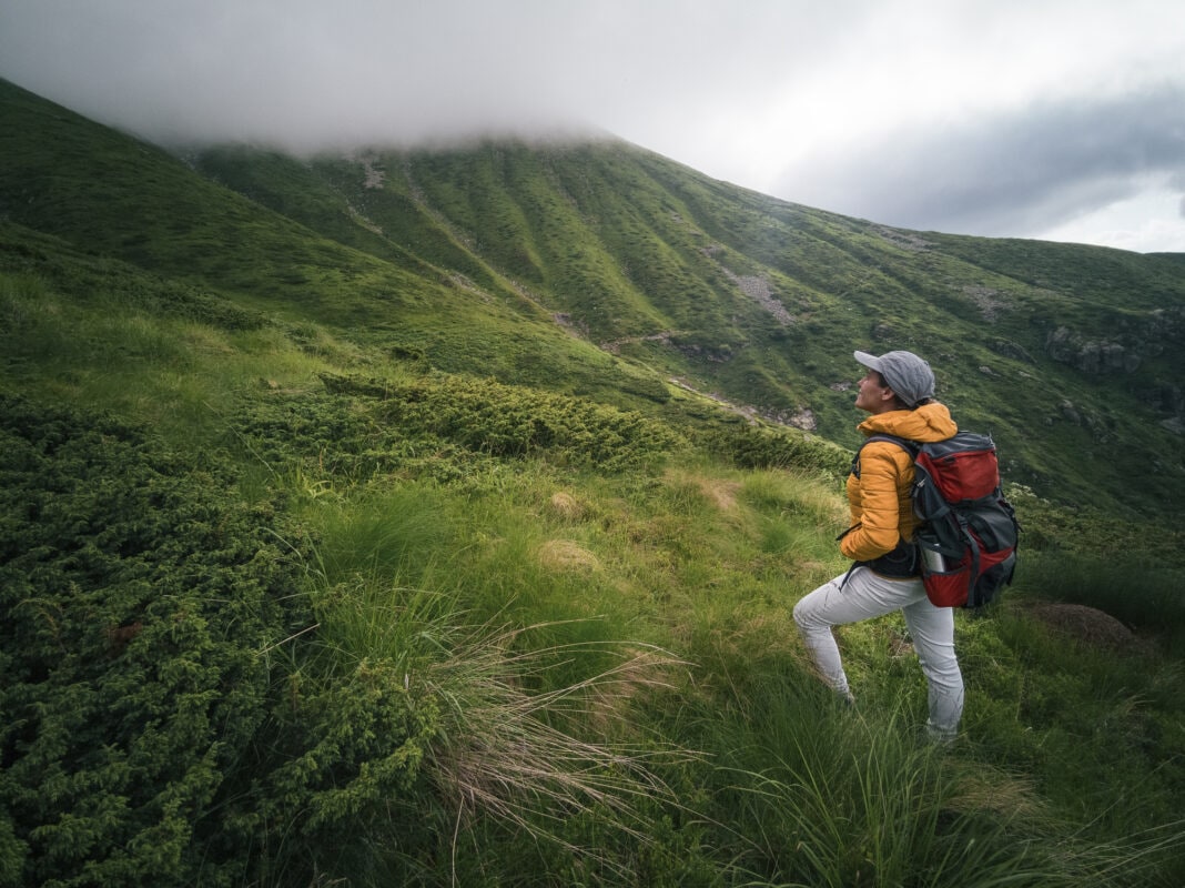 Back to Nature. Woman solo traveler hiking in the mountains. Enjoyment outdoors on a sunny day after the COVID-19 pandemic.