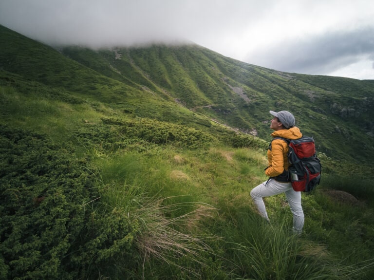 Back to Nature. Woman solo traveler hiking in the mountains. Enjoyment outdoors on a sunny day after the COVID-19 pandemic.