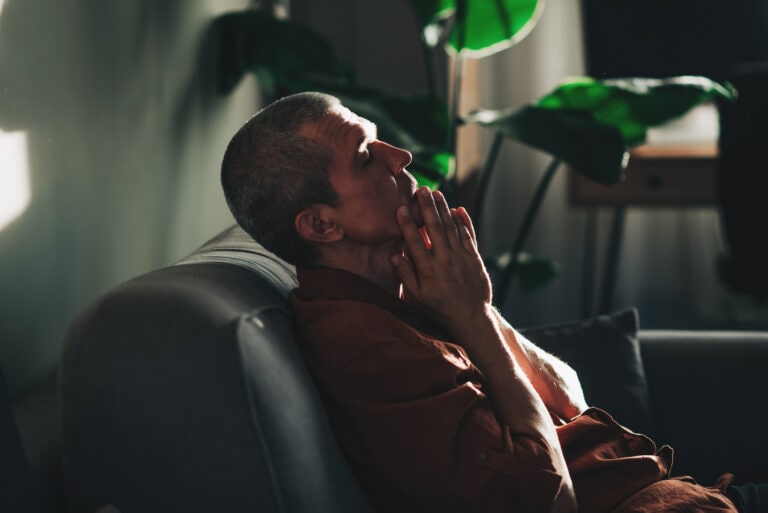 Unpleasant pain. Sad unhappy handsome man sitting on the sofa and holding his forehead while having headache