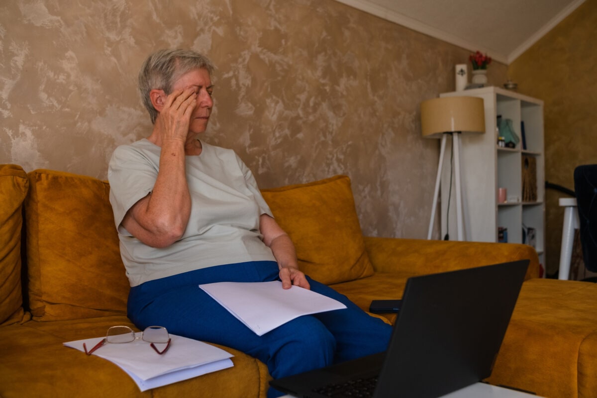 dry eye syndrome. Woman senior rubs her eyes, tired after working at home on a laptop