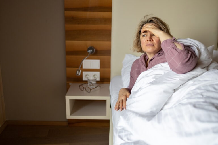 Depressed mature woman suffering from headache while lying in bed at home