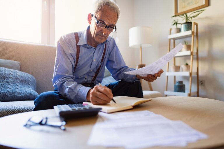 Low-angle view of a senior man going over his finances at home and analyzing bills while writing in a planner