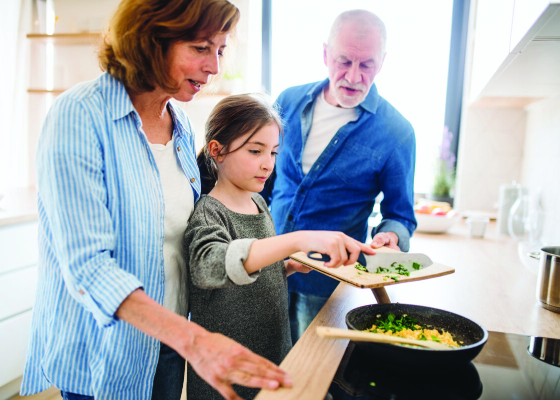 Senior grandparents and granddaughter preparing food indoors in kitchen.
