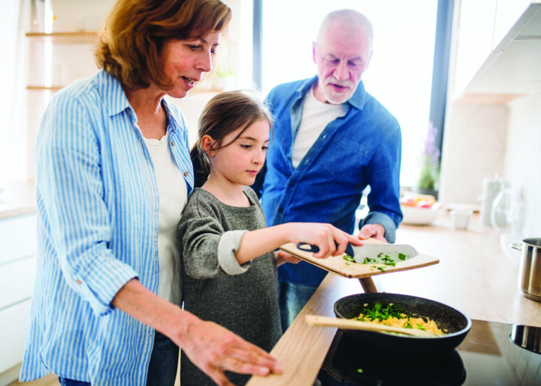 Senior grandparents and granddaughter preparing food indoors in kitchen.