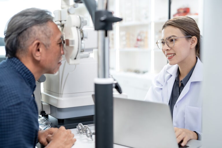 Assesment Of Visual Function an Eye Refraction Test. A female opthamologist uses a manual phoroptor to measure the refractive error and determine the eyeglass numbers of senior male patient in an ophthalmology clinic.