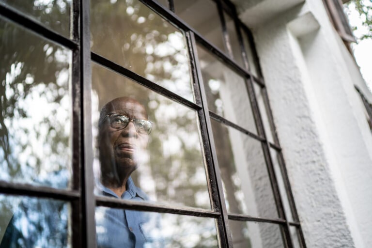 Senior man looking through the window at home