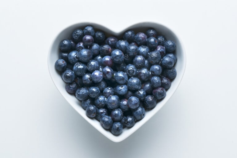 Blueberries in heart-shape bowl on white background