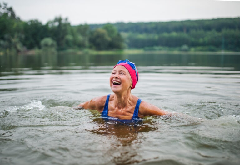 Active senior woman standing in lake outdoors in nature, laughing.