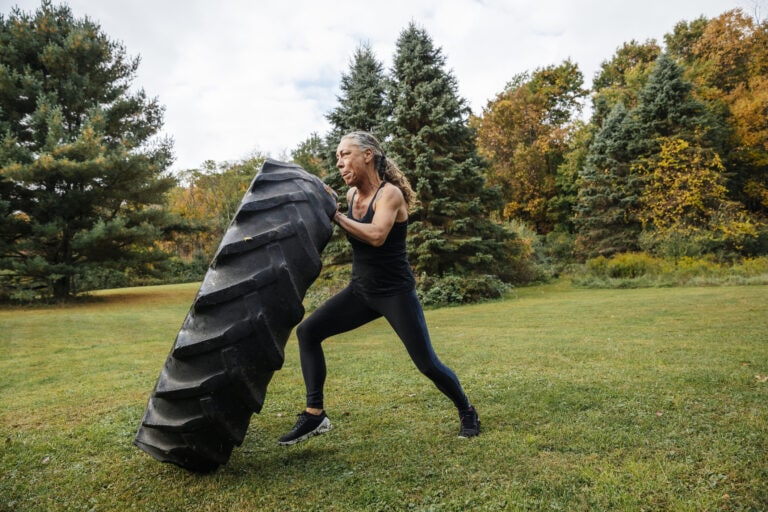 Strong woman pushing tire while exercising in backyard