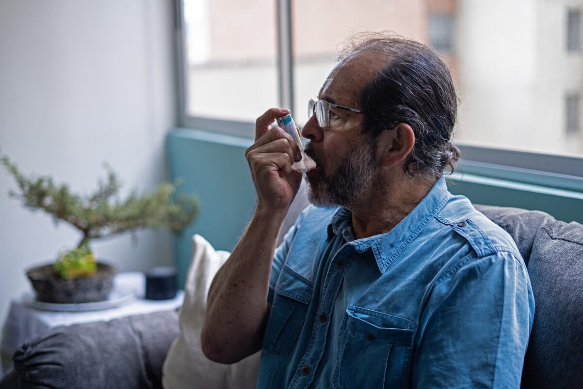 Older male asthma sufferer using an inhaler at home.