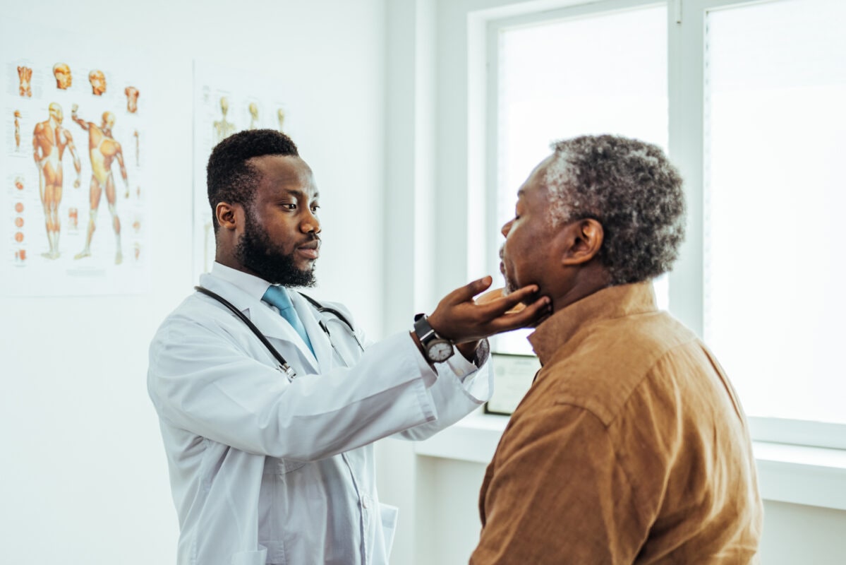Male otolaryngologist touching lymph nodes on neck and examining throat of male patient during medical checkup