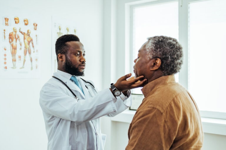 Male otolaryngologist touching lymph nodes on neck and examining throat of male patient during medical checkup