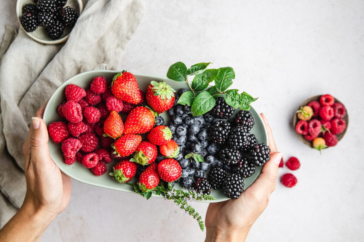 Point of view of a woman hands holding plate of berries on white table