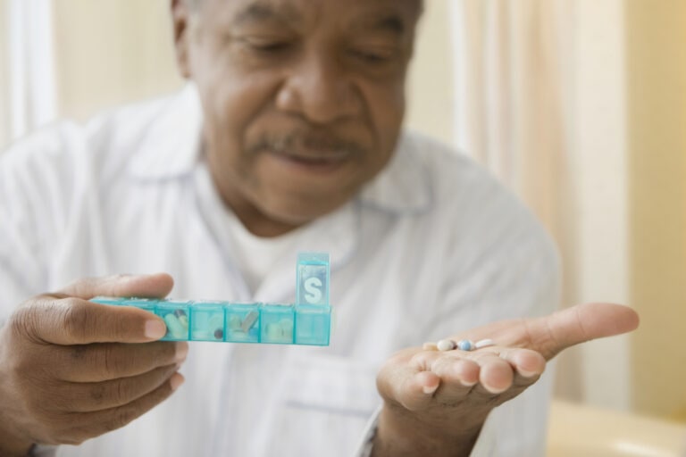 African man holding daily pill box with pills