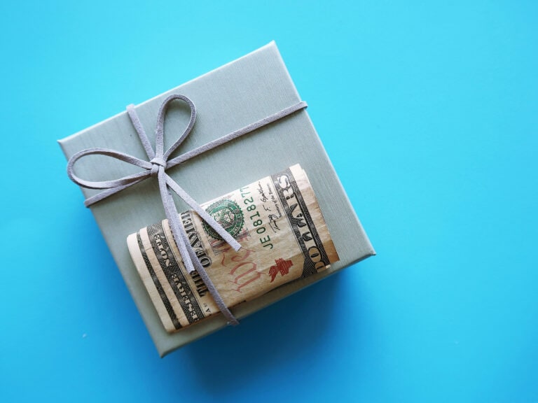 Grey gift box with cash dollars money on blue copy space background, concept of money gift giveaway or bonus to employees at year-end Christmas Holiday season
