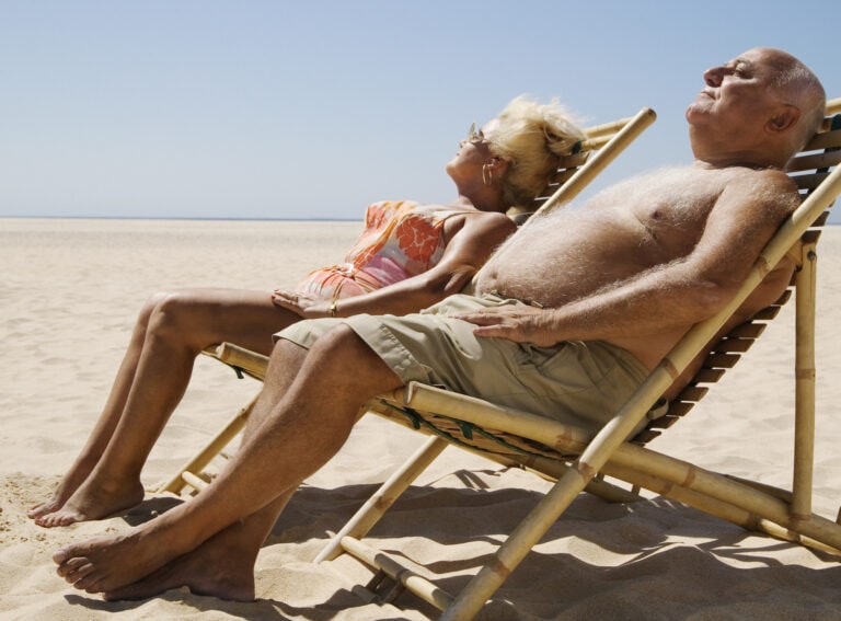 Senior couple sitting in chairs on beach, eyes closed
