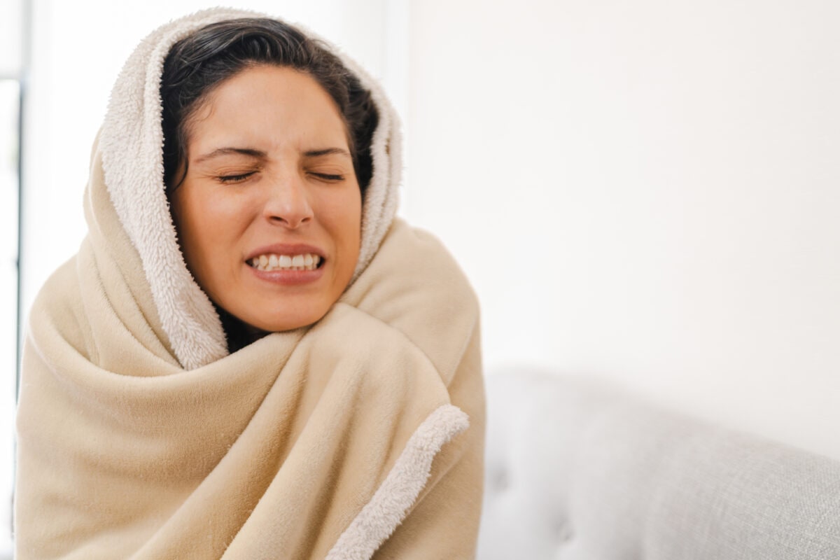Cold woman covered with a blanket sitting on the sofa