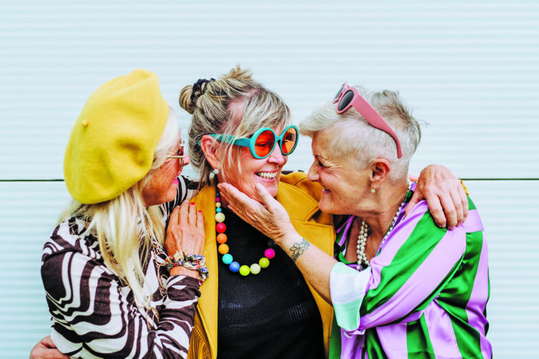 Portrait of happy three senior friends in colourful clothes.