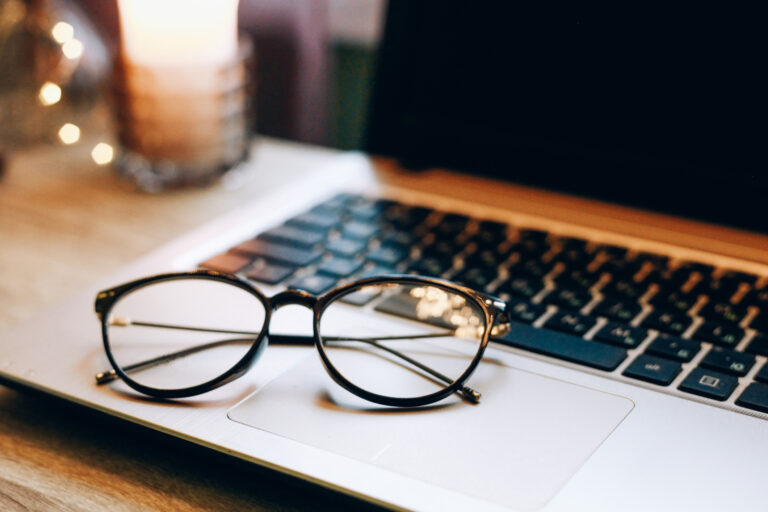 Close up of eyeglasses, blurred laptop and cup home interior details. Online shopping, work and study from home concept.
