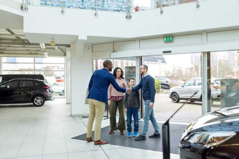 Automobile dealer shaking hands with family visiting a car showroom