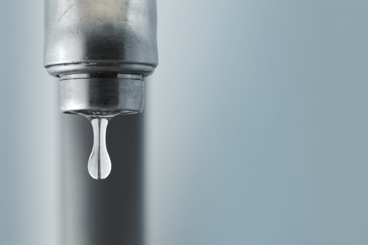 Sink faucet dripping with the water drop in focus