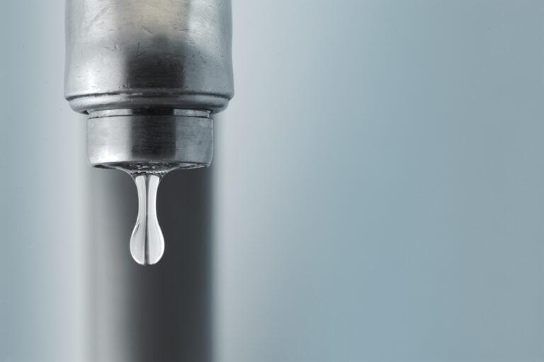 Sink faucet dripping with the water drop in focus