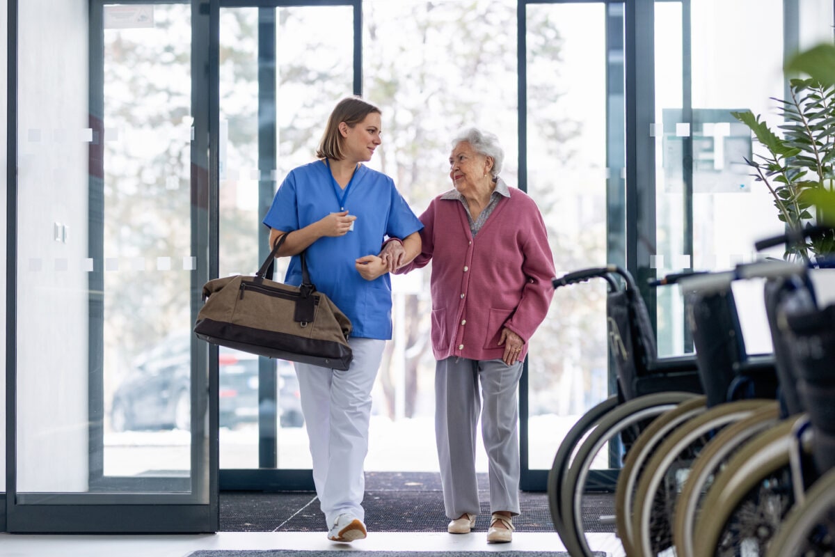 Nurse helping senior woman with bag, coming for planned surgery. Worried senior patient talking with nurse. Emotional support from healthcare workers for elderly woman.