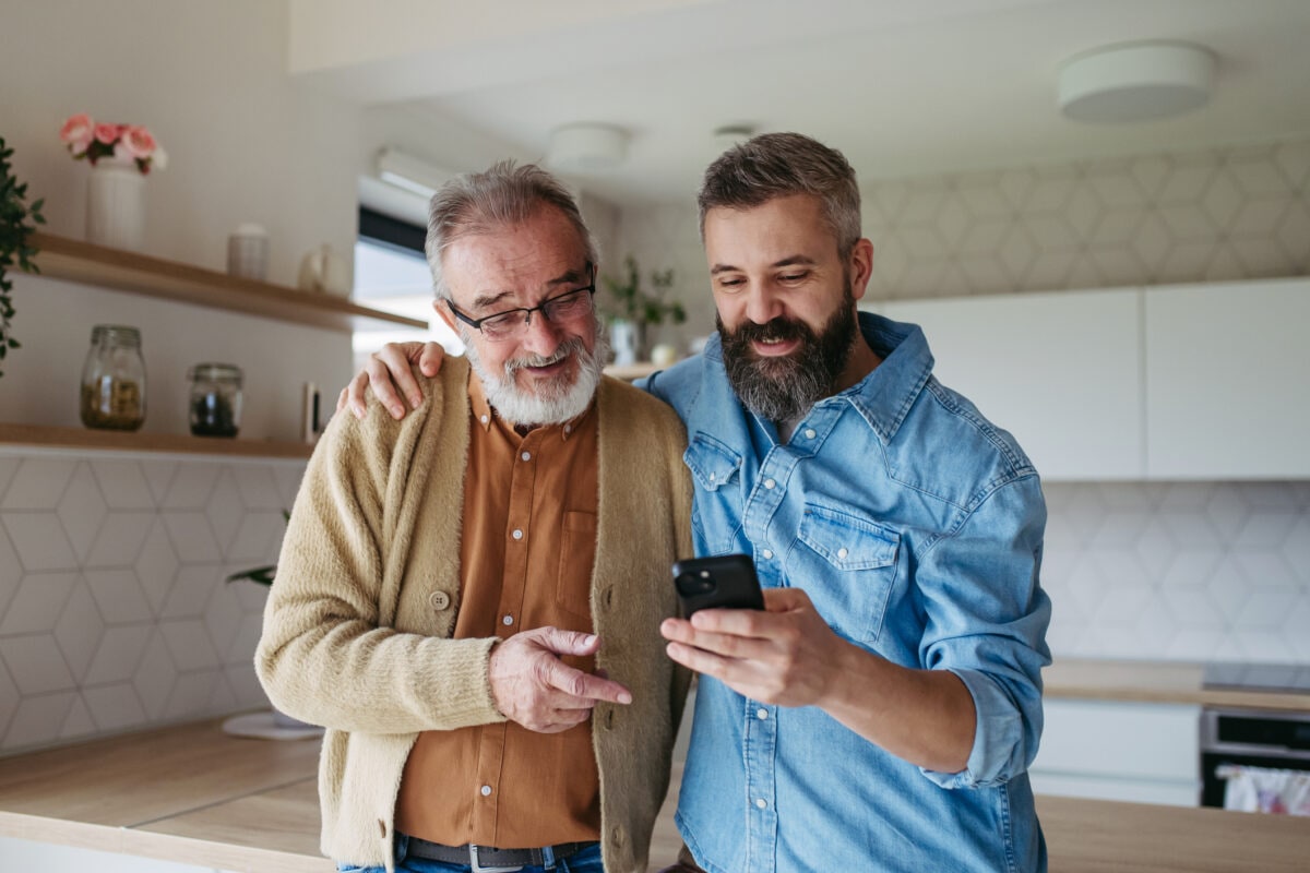 Mature son showing dad photos of his family in smartphone, making video call.