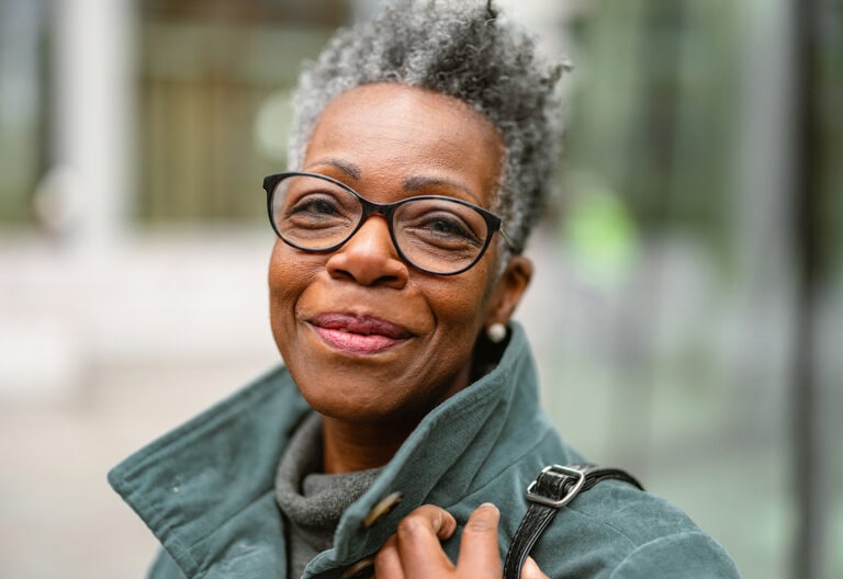Woman with gray hair wearing glasses and green jacket smiling at the camera