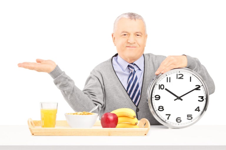 Senior gentleman with clock and breakfast tray gesturing