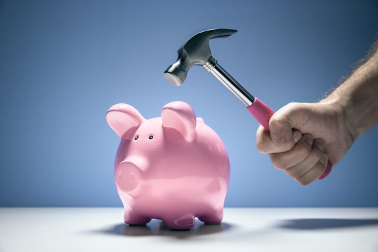 Piggy bank and hand with hammer about to smash to get at savings