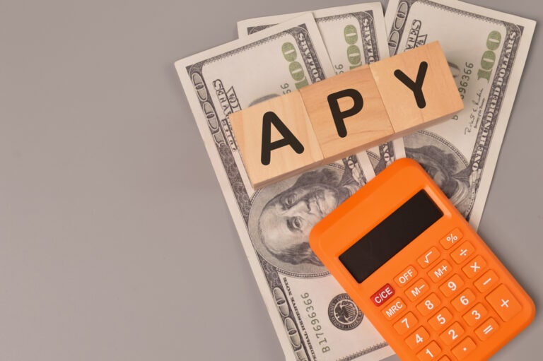 Money banknotes, calculator and wooden blocks written with APY stands for ANNUAL PERCENTAGE YIELD.