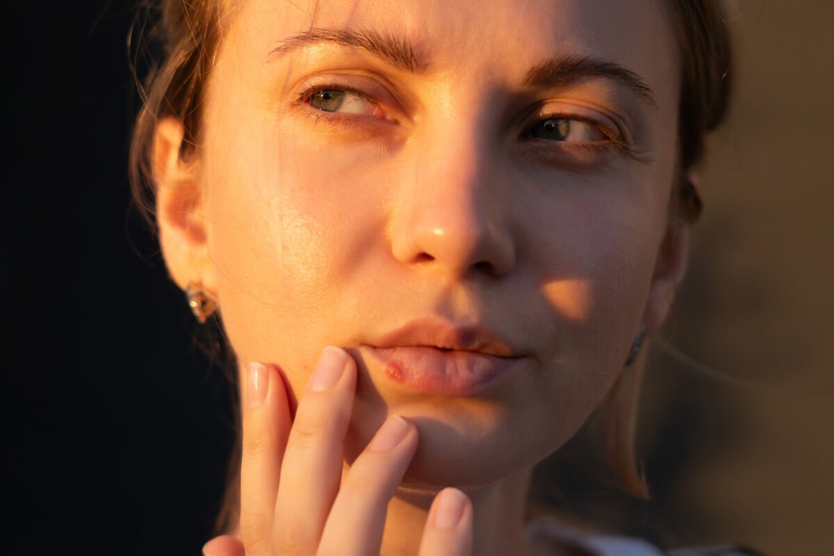 Close up of girl's lips with herpes touching with finger. Beauty dermatology concept
