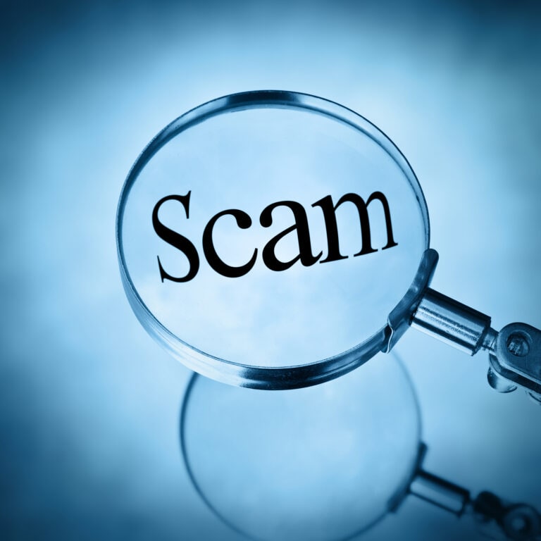 A magnifying glass examines the word scam illustrating the need to detect and avoid scams in this modern world.